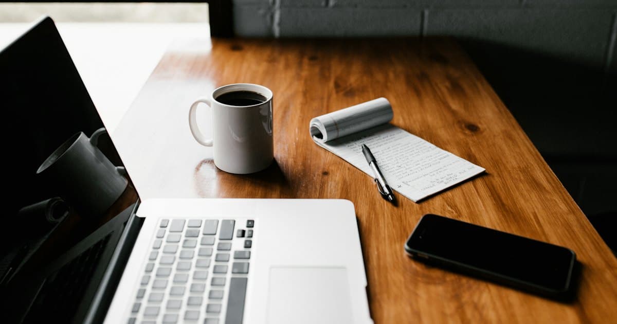 Notebook, celular e café sobre a mesa de trabalho