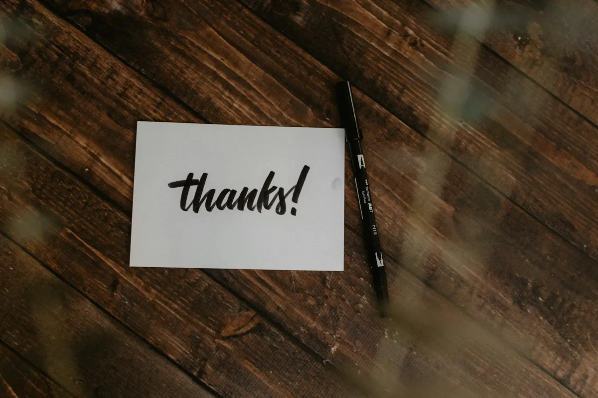 Cartão escrito "thanks" sobre uma mesa de madeira