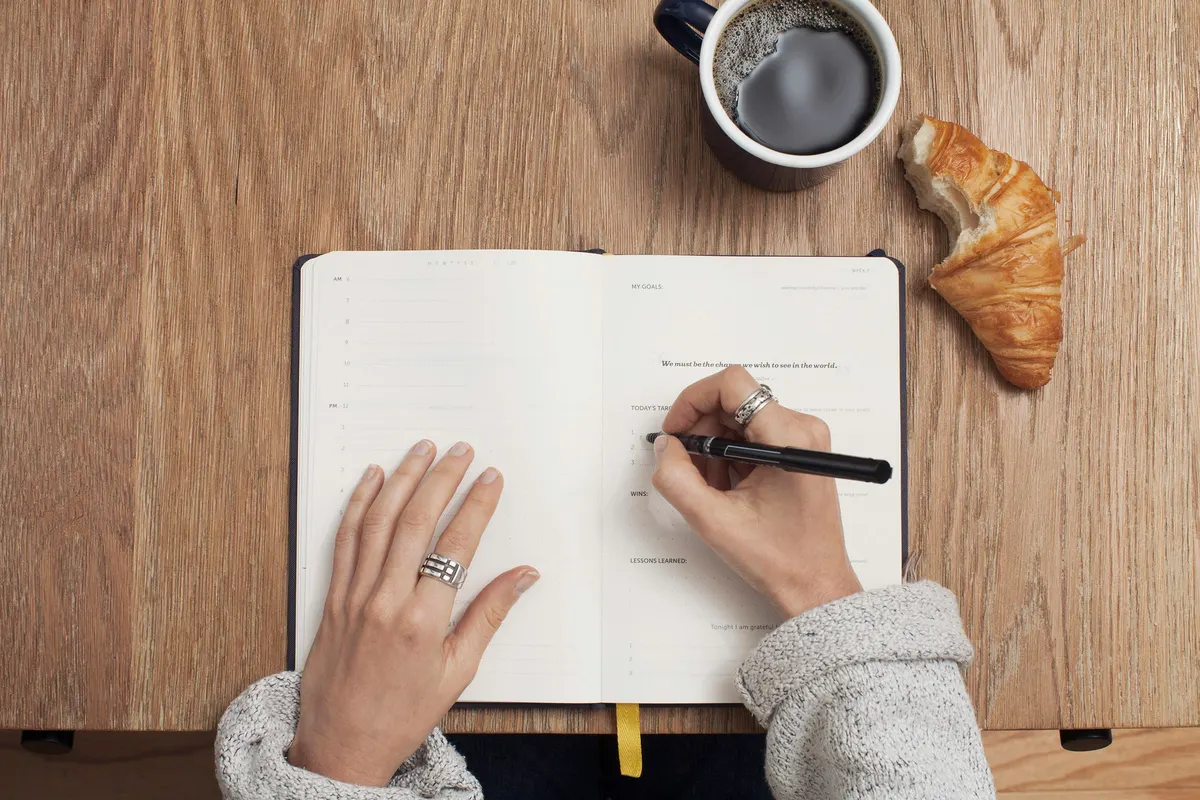 Mão escrevendo em uma agenda aberta