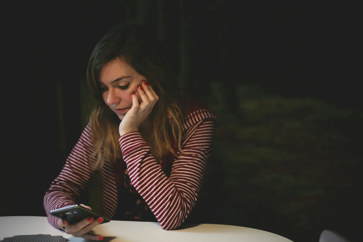 Mulher pensativa lendo uma mensagem no celular