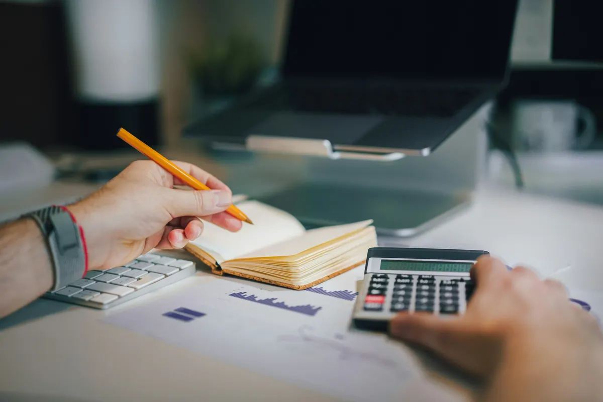 Mãos fazendo anotações ao lado de uma calculadora